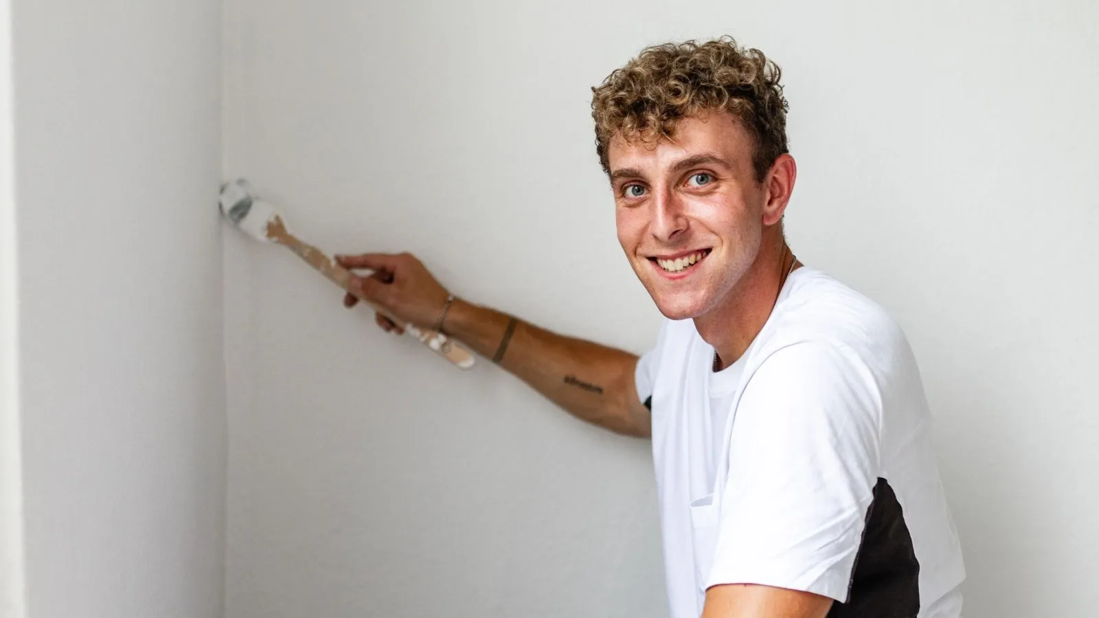 Foto von Maler und Lackierer Dennis Schmidt während er eine Wand streicht.